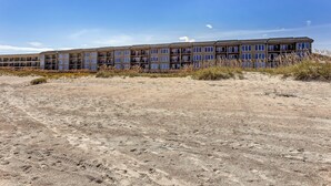 Un hotel de varios pisos con techo plano y ventanas amplias, ubicado en terreno arenoso con vegetación escasa.