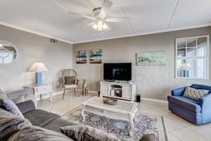 Relax in this inviting space with a flat-screen TV, comfortable seating, and decorative tropical art.