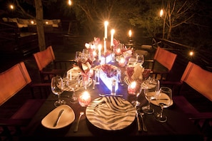 An outdoor dining area with tables set for a meal, candles, and a zebra-patterned centerpiece. - Naledi Game Lodges (Hoedspruit)