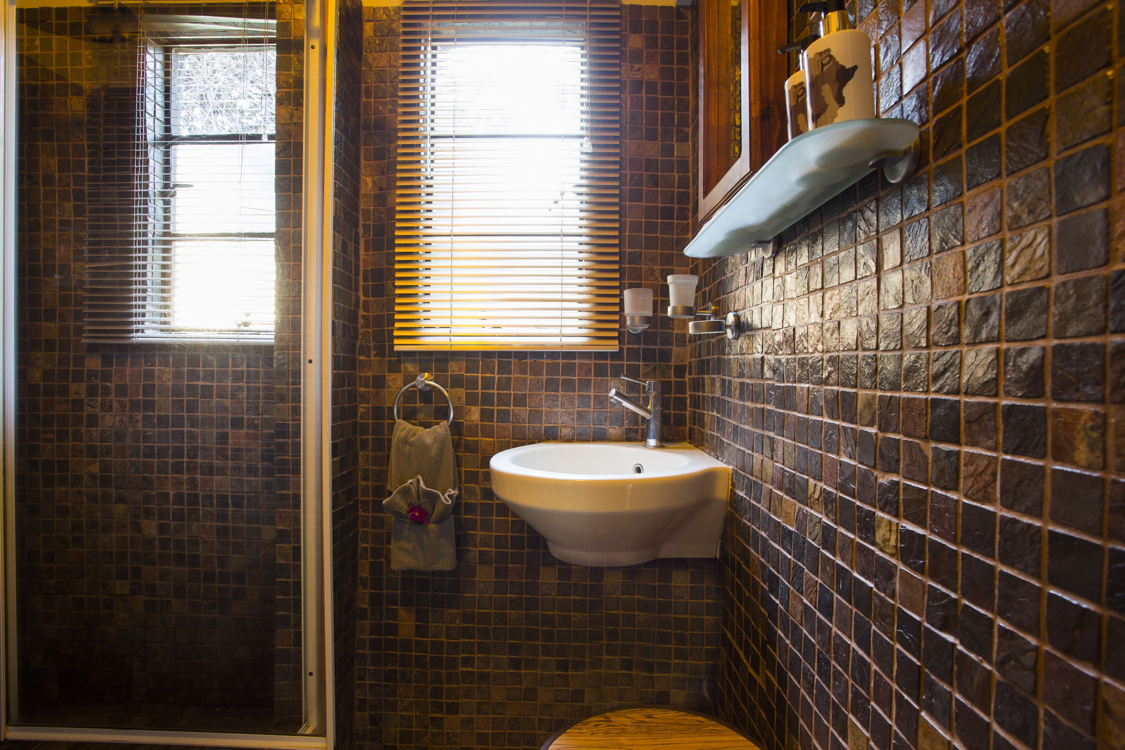 A bathroom with a tiled wall, a sink, and a window with blinds.