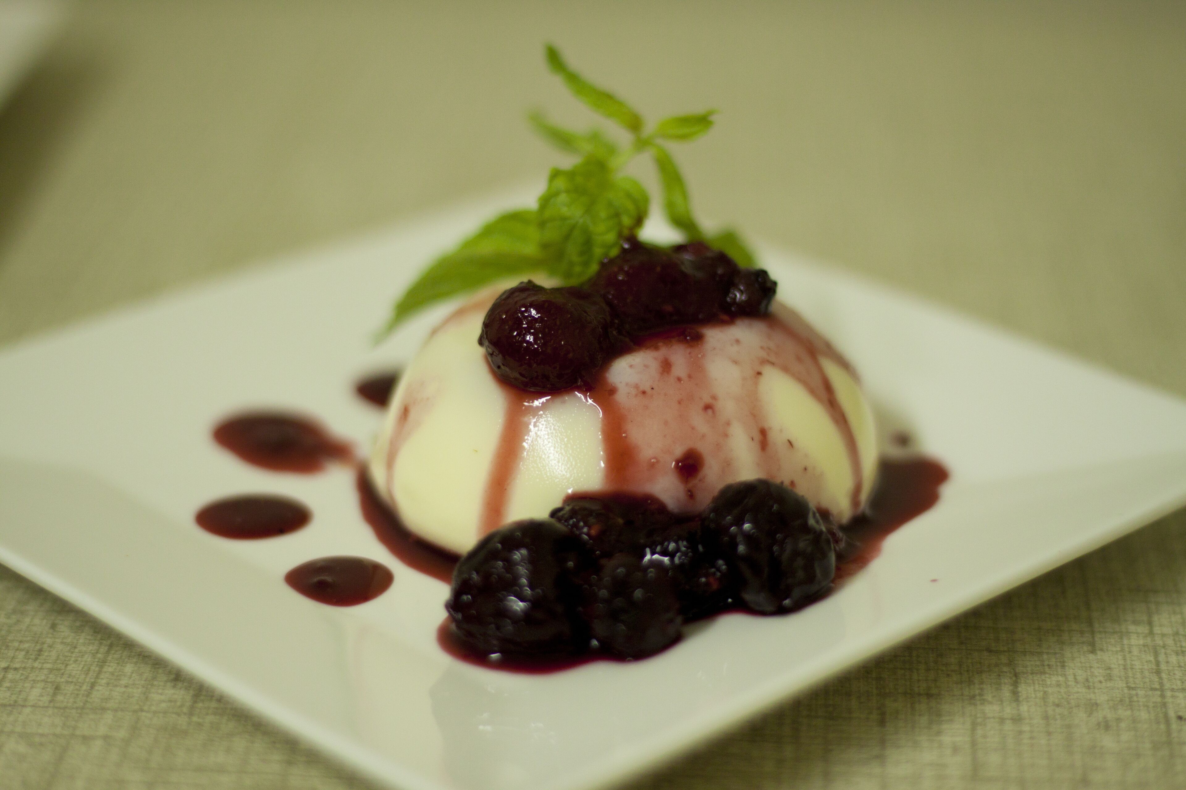 Een dessert op een wit bord, met bessen en een muntblaadje.