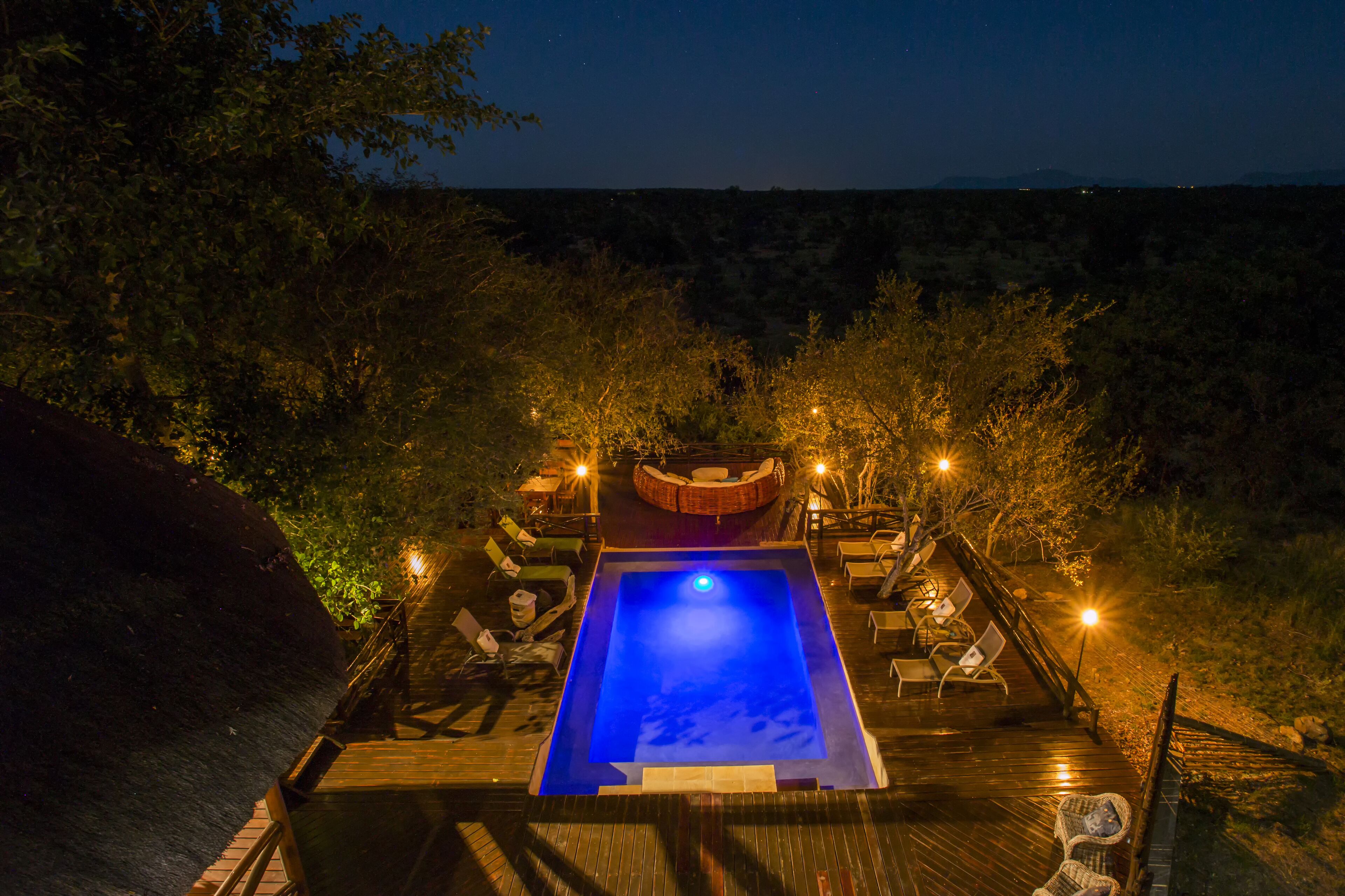 A swimming pool with a wooden deck, surrounded by lounge chairs and a seating area with a fire pit.