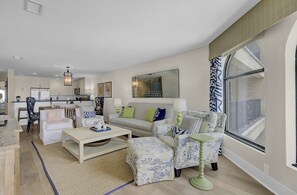 A spacious living room with a sofa set, a coffee table, and a dining area with a kitchen in the background.