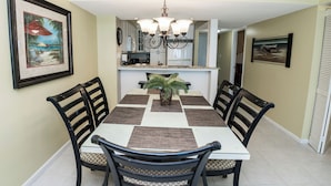 A dining area with a table, chairs, a chandelier, and a kitchen in the background.