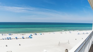 A beach with white sand and clear turquoise water. There are several umbrellas and lounge chairs along the shore.