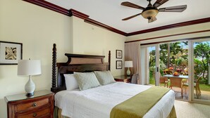 A hotel room with a large bed, a wooden headboard, a ceiling fan, a nightstand with a lamp, and a view of a garden through a sliding glass door. - Waipouli Beach Resort Luxury Garden Ground Floor! AC Pool (Kapaa)