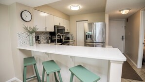 Una cocina moderna con encimera blanca, electrodomésticos de acero inoxidable y taburetes de bar verdes.