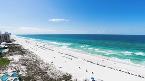 Una playa de arena blanca, un océano azul transparente y algunos edificios al fondo.