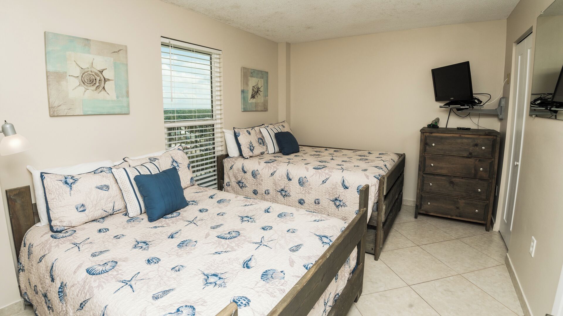 A bedroom with two beds, a dresser, a TV, and artwork on the walls.