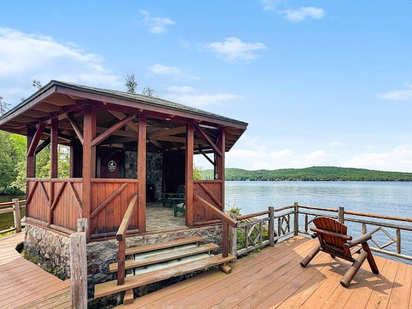 A wooden cabin with a porch, a chair, and a view of a lake.
