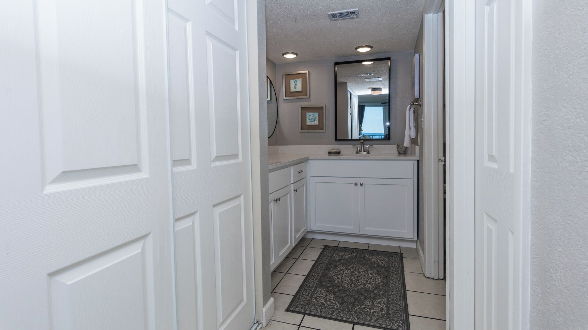 A narrow hallway leading to a bathroom with white cabinetry, a sink, and a mirror.