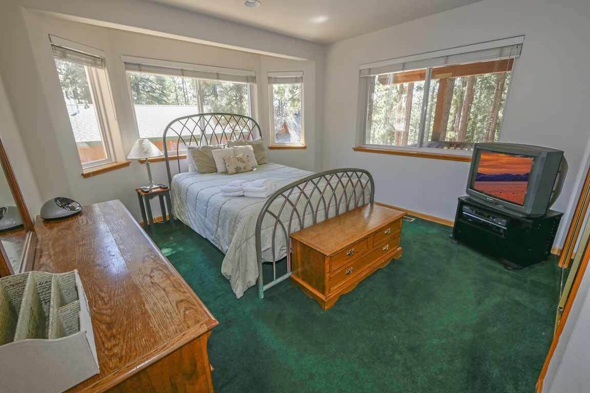 Une chambre à coucher comprenant un lit, une commode en bois, un bureau, une télévision et de grandes fenêtres.
