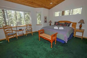 A bedroom with a large bed, two bedside tables with lamps, a wooden bench, and two chairs.