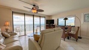 Ein geräumiges Wohnzimmer mit Balkon, Deckenventilator, Fernseher und Essbereich mit Korbstühlen.