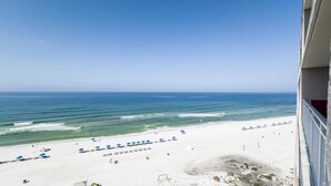 A beach with white sand, blue umbrellas, and a view of the ocean.