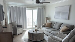 A modern living room with a grey sofa, two armchairs, a coffee table, and a TV on a wooden cabinet.