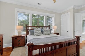 Un dormitorio con cama de madera, dos mesitas de noche con lámparas, una ventana con persianas y una puerta.