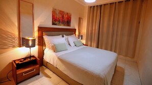 A neatly made bed with white linens, a wooden nightstand with a lamp, a painting on the wall, and a large window with curtains. - Cozy Studio welcoming you (Casablanca)