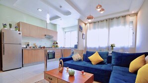 A modern living room with a blue sofa, a wooden coffee table, and a kitchen area with wooden cabinets and a refrigerator. - Cozy Studio welcoming you (Casablanca)