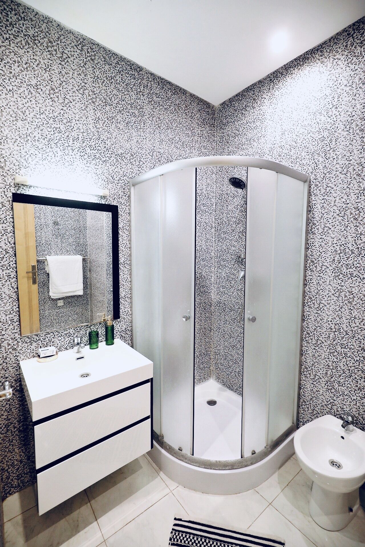 Un baño con tocador blanco, ducha con mampara de vidrio y lavabo blanco.