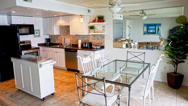 A modern kitchen with white cabinets, a black refrigerator, and a glass dining table with chairs. - Thunder Island 128C-Baywater 39th St, Free WiFi, Pool, Elev, W/D, AC (Ocean City)