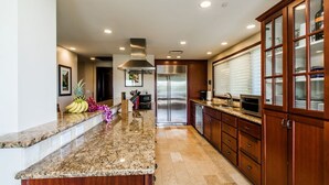 A modern kitchen with granite countertops, stainless steel appliances, wooden cabinetry, and a central island.