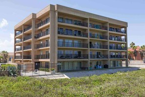 A multi-story building with balconies, a gated entrance, and a landscaped area in front.