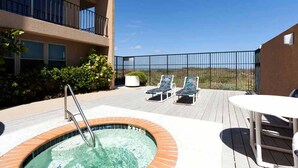 Zona de piscina en la azotea con jacuzzi, sillas de descanso y una mesa.