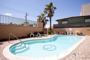 A swimming pool with lounge chairs, palm trees, and a building in the background.