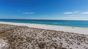 A beach with a wooden boardwalk leading to the shore, clear blue sky, and calm sea.