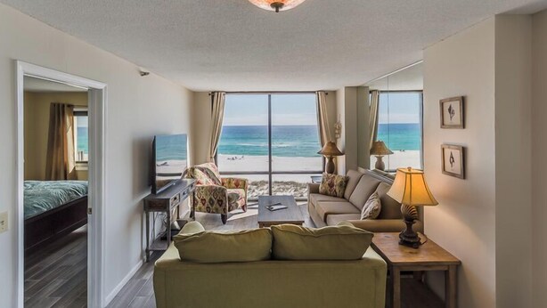 A room with a bed, a sofa, a TV, a lamp, and a view of the beach.