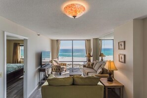 Una habitación con cama, sofá, televisión, lámpara y vista a la playa.