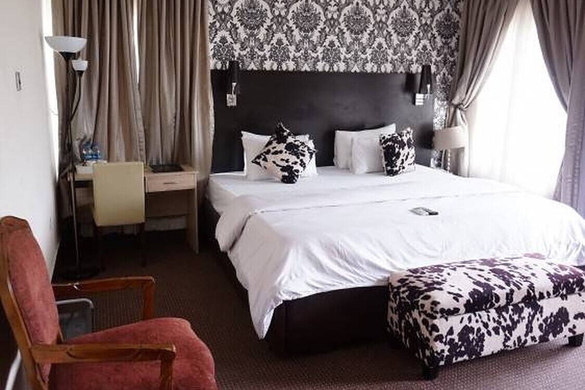 A hotel room with a large bed, a desk, a chair, and a patterned wallpaper.