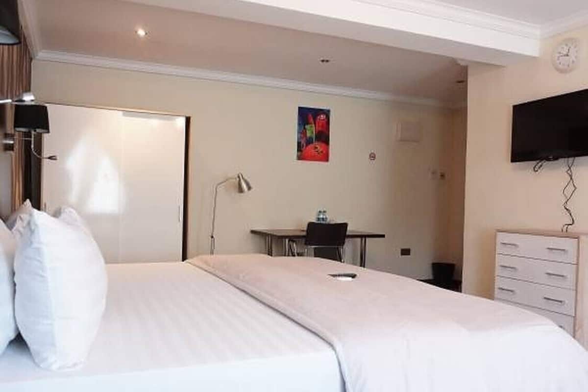 A hotel room with a large bed, a desk, a chair, a TV, and a dresser.