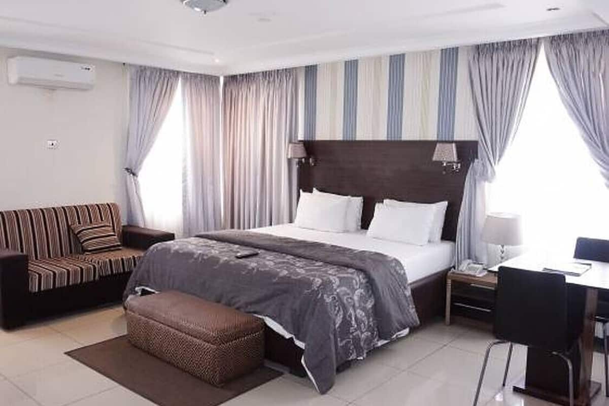 A modern hotel room with a large bed, a sofa, a desk, and a chair.