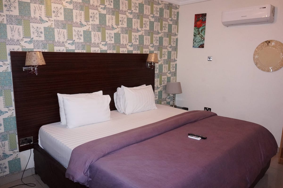 A neatly made bed with a purple bedspread, two bedside lamps, and a wall-mounted air conditioner.