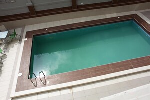 Piscina interior retangular com borda em azulejo castanho e superfície de água azul cristalina.