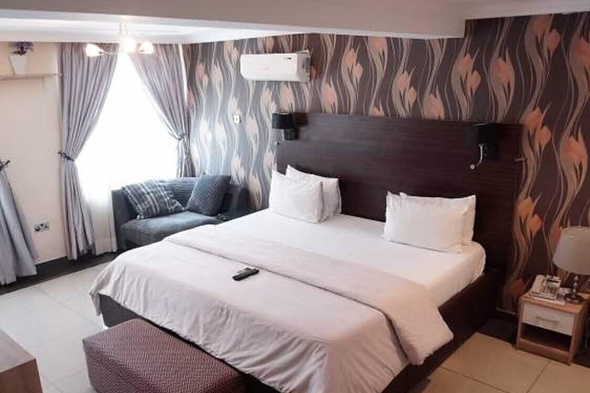A hotel room with a large bed, a bedside table, a chair, and a window with curtains.