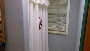 A bathroom with a shower curtain, a window with blinds, and a green door frame.