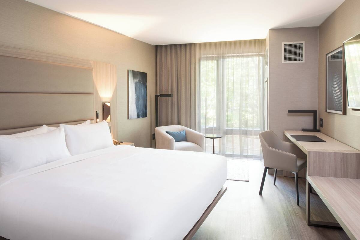 A hotel room with a large bed, a desk, a chair, and a window with curtains.