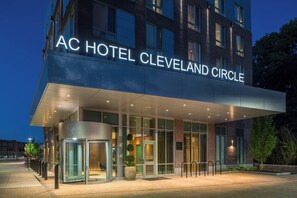 The exterior of the AC Hotel Cleveland Circle with a modern design, large glass entrance, and a well-lit facade.