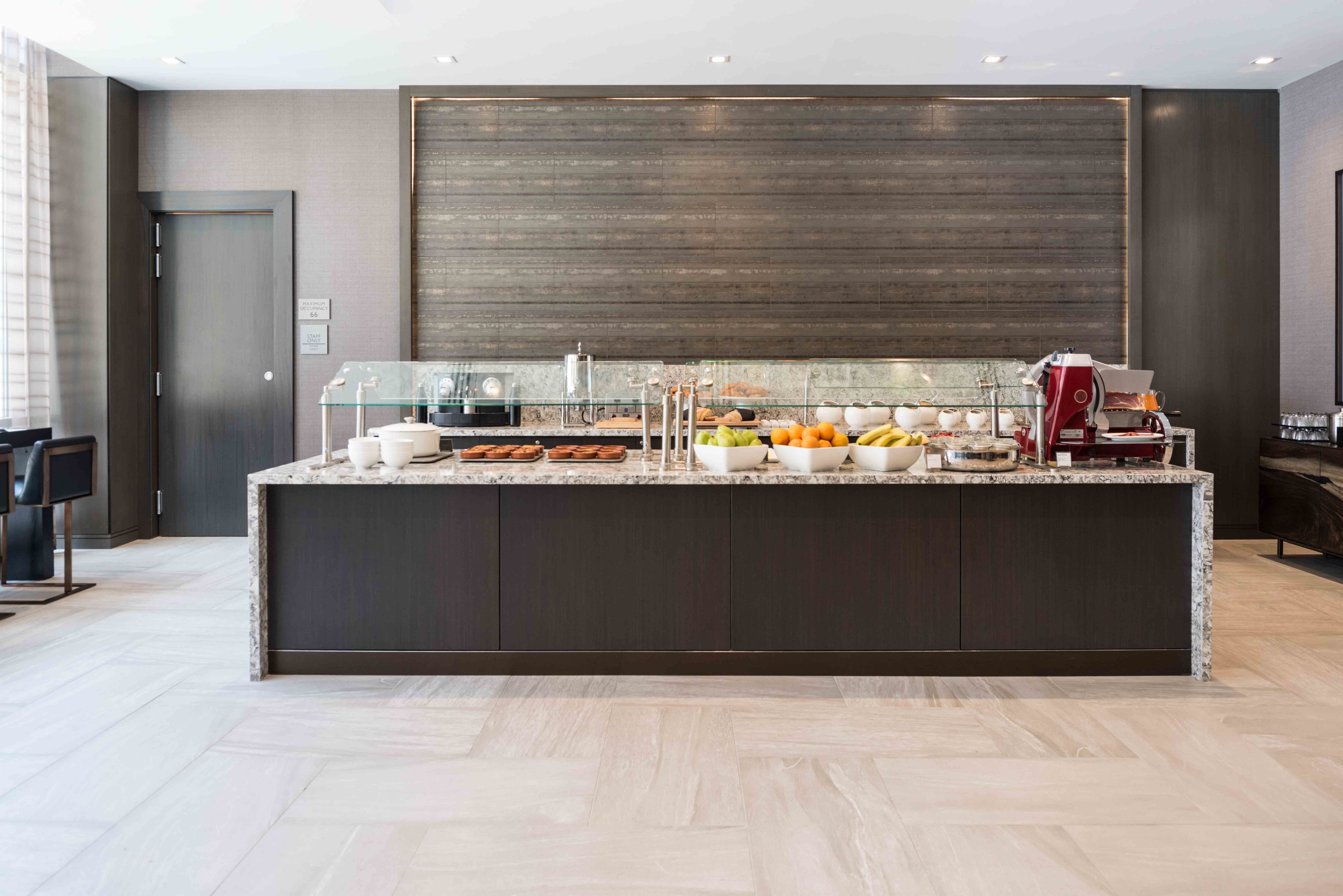 A modern kitchen with a marble countertop, a coffee machine, and various fruits and vegetables.