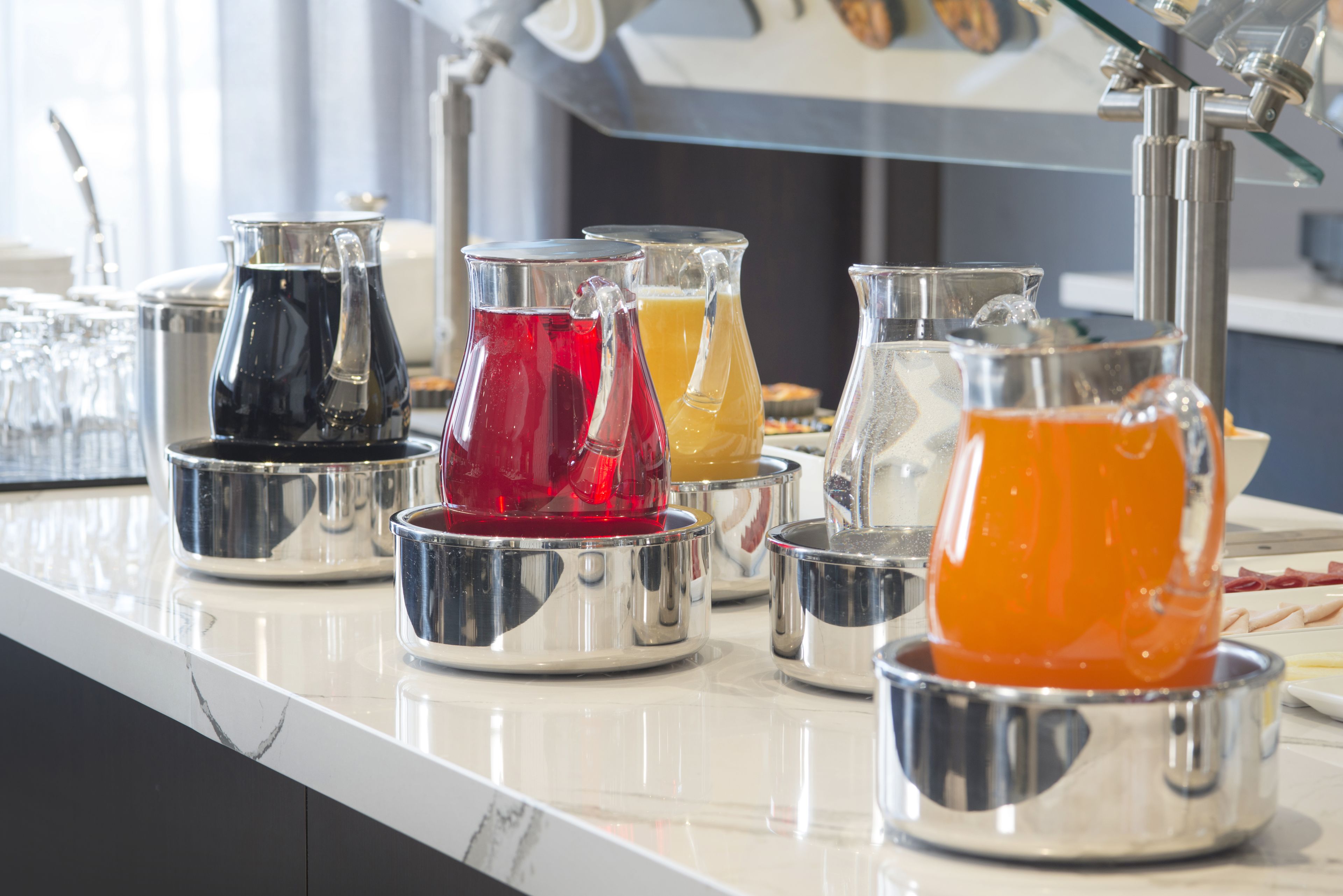 A bar area with multiple pitchers of colorful beverages on a marble countertop.
