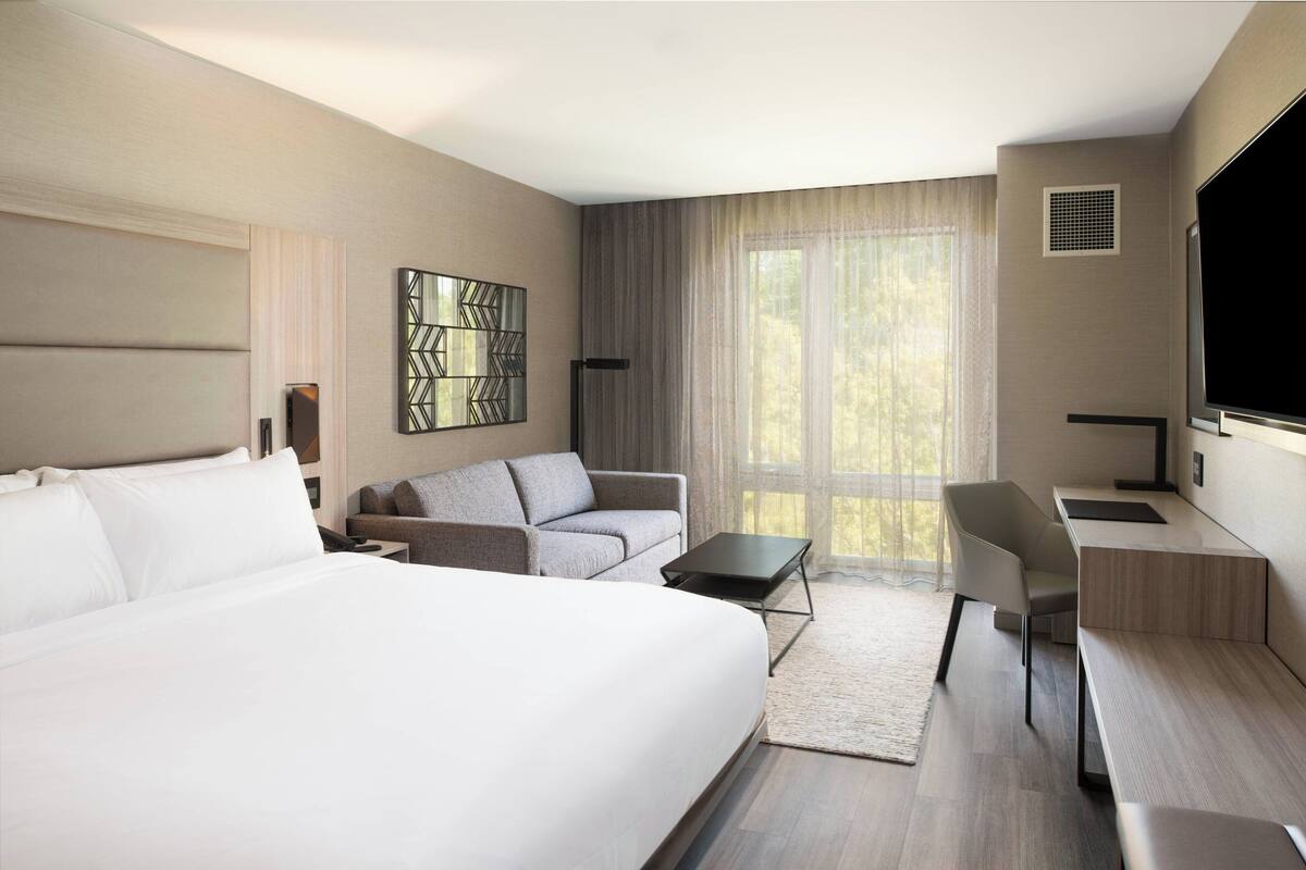 A modern hotel room with a large bed, a sofa, a desk, and a TV.