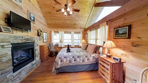 Cozy cabin room with a stone fireplace, comfortable bed, and wooden nightstand.