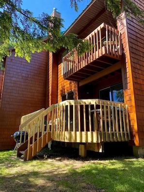 A wooden deck with a staircase leading to a second-story balcony.