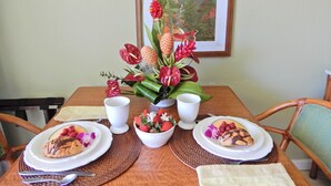 A dining table with two plates of food, two white cups, and a floral centerpiece.