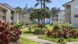 A resort with multiple-story buildings, a well-maintained garden with tropical plants, and a clear view of the ocean.