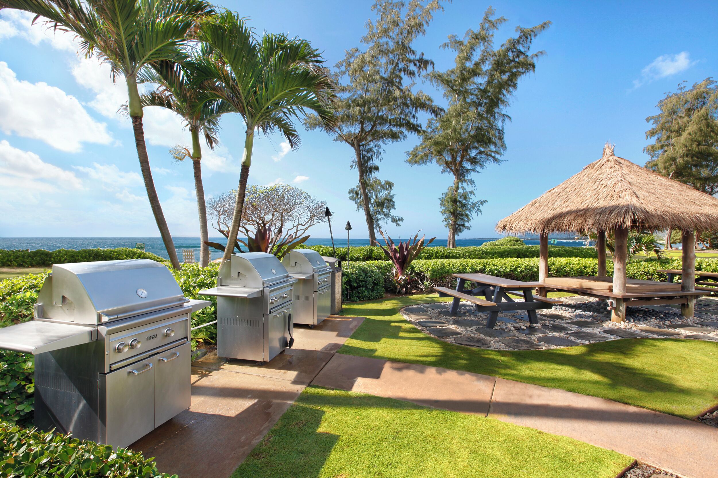 An outdoor patio with a grill, picnic table, and thatched gazebo.