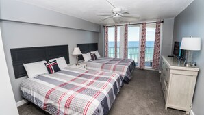 Une chambre d’hôtel avec deux lits, un ventilateur de plafond, un balcon avec des rideaux, un bureau avec une lampe et une télévision.